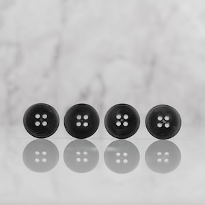 May include: Four black buttons with four holes each, arranged in a row on a white marble surface.