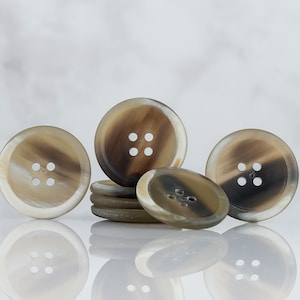 May include: A group of five brown and white horn buttons with four holes each. The buttons are arranged in a semi-circle with one button in the center and two on each side.