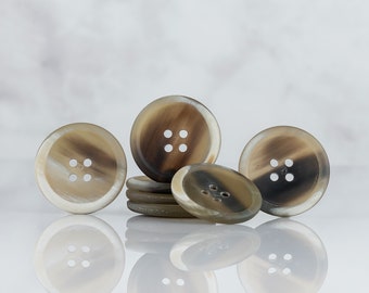 May include: A group of five brown and white horn buttons with four holes each. The buttons are arranged in a semi-circle with one button in the center and two on each side.