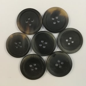 Peut inclure: Sept boutons en corne brun et noir avec quatre trous chacun. Les boutons ont un bord surélevé et une surface lisse.