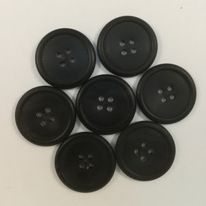 Może przedstawiać: Siedem czarnych plastikowych guzików z czterema otworami każdy.
