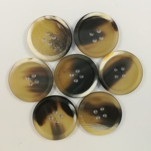 May include: Seven round buttons with four holes each, arranged in a circular pattern. The buttons have a marbled appearance, with shades of brown, tan, and cream. The buttons are made of a smooth, glossy material.