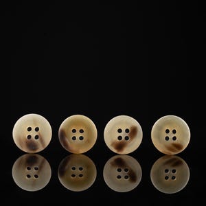 Pode incluir: Quatro botões marrons e bege com quatro furos cada, dispostos em fila sobre um fundo preto. Os botões são refletidos na superfície.