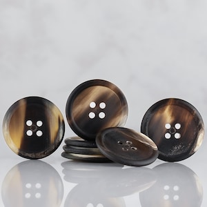 May include: Four brown and black horn buttons with four holes each. The buttons are arranged in a semi-circle with one button in the center.