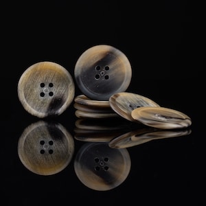 May include: A group of four brown and black horn buttons with four holes each. The buttons are stacked on top of each other.