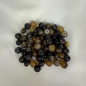 Puede incluir: Un mont&oacute;n de cuentas de cuerno de color marr&oacute;n y negro. Las cuentas son redondas y tienen un agujero en el centro. Son perfectas para hacer joyas u otras manualidades.
