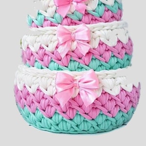 Puede incluir: Conjunto de cuatro cestas de crochet en rosa, blanco y verde con lazos de satén rosa.