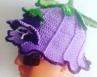 May include: Purple crocheted hat shaped like a flower with green leaves. The hat has a ruffled edge and a flower detail on the side.