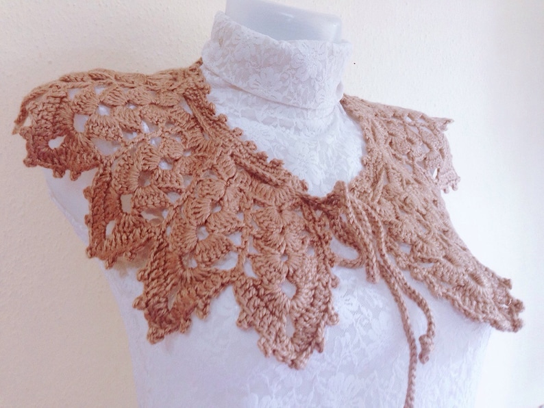 May include: A brown crocheted collar with a delicate floral pattern. The collar has a tie at the back.