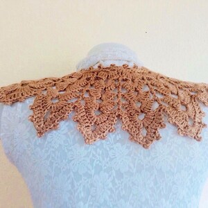 May include: A crocheted collar in a light brown color. The collar is made of delicate, intricate stitches and has a scalloped edge.