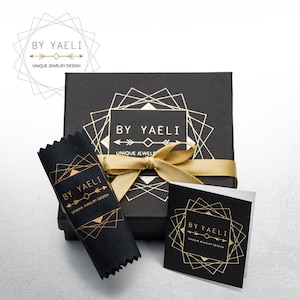 May include: A black jewelry box with a gold geometric design and the text "BY YAELI UNIQUE JEWELS" on the lid. The box is tied with a gold ribbon and comes with a black velvet pouch with the same design and text.