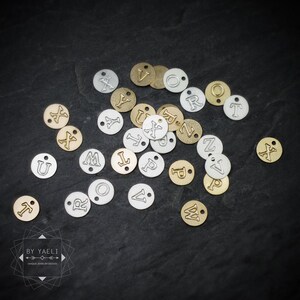 Small round gold-tone and silver-tone charms stamped with individual letters are scattered across dark slate.