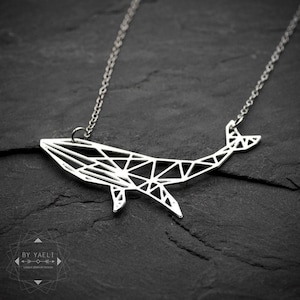 Silver-tone geometric whale pendant with angular openwork lines and two downward fins, hanging from a fine chain on dark slate.