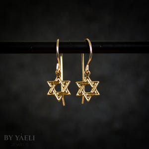 May include: A pair of gold-toned Star of David dangle earrings. The earrings are suspended from a thin gold-toned wire.