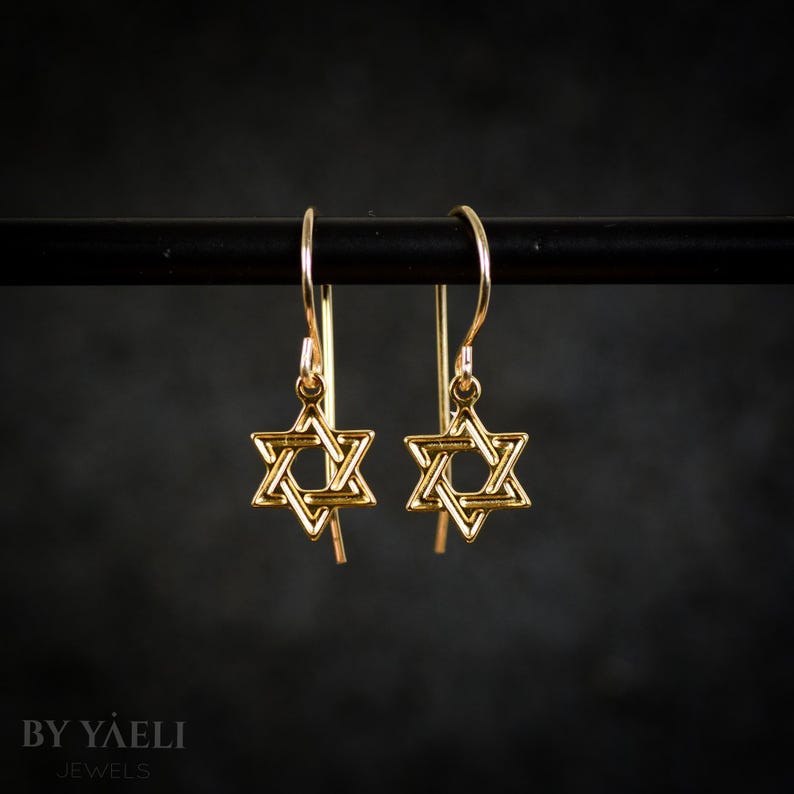 May include: A pair of gold-toned Star of David dangle earrings. The earrings are suspended from a thin gold-toned wire.
