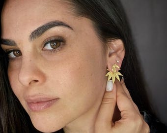 May include: A gold-toned earring featuring a detailed toucan bird perched atop a cluster of tropical leaves. The earring has a polished metallic finish and is worn on the earlobe, showcasing a distinct avian and botanical design element.