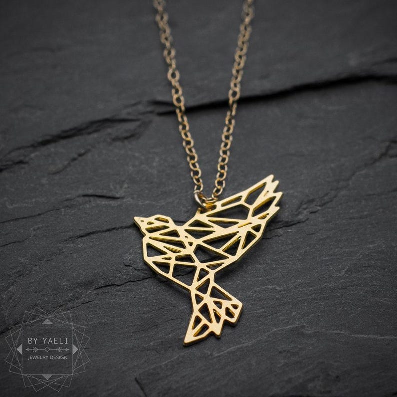 Gold-toned openwork bird pendant on dark slate, with an upraised wing, pointed tail and a geometric pattern of triangular cutouts.