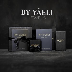 Black textured ByYaeli jewelry boxes and dark branded cards arranged on a dark surface, with black satin bows on two boxes.