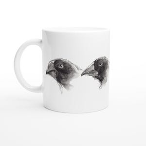 May include: White ceramic mug featuring a black and white illustration of two bird profiles. The artwork showcases detailed shading and highlights, creating a realistic depiction of the birds' heads and beaks. The mug has a curved handle.