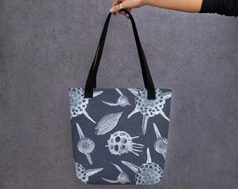 May include: A black tote bag with a pattern of white, detailed illustrations of microscopic sea creatures on a dark blue background.