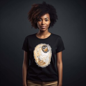 Peut inclure: Un t-shirt noir avec une illustration aquarelle d'une cellule sur le devant. La cellule est de couleur brun clair avec un noyau brun foncé.