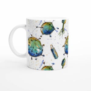 Könnte beinhalten: Weiße Keramiktasse mit einem Aquarelldesign aus farbenfrohen, abstrakten Virusillustrationen in Blau, Grün und Gelb. Die Tasse hat einen weißen Henkel und ist für heiße oder kalte Getränke geeignet. Das Design umfasst blaue und gelbe Spritzer.