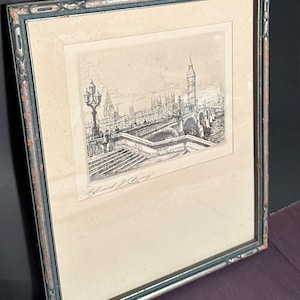 May include: A black and white etching of the Houses of Parliament and Big Ben in London, England. The etching is framed in a dark wood frame with a silver-colored mat. The artist's signature is visible in the lower left corner.