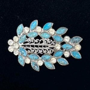 May include: A silver-toned hair clip with a floral and leaf design. The clip features turquoise-colored stones and clear crystals. The clip is approximately 3 inches long and 1.5 inches wide.
