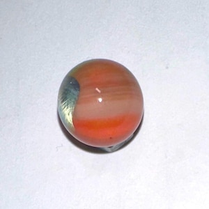 May include: A close-up of a colorful marble. The marble is primarily orange, with bands of white and a touch of yellow and blue. The glass marble is a sphere, and the colors blend together.
