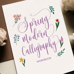 May include: A white workbook with the words "Spring Modern Calligraphy" in purple script, decorated with small floral illustrations. The word "WORKBOOK" is at the bottom in a smaller font.
