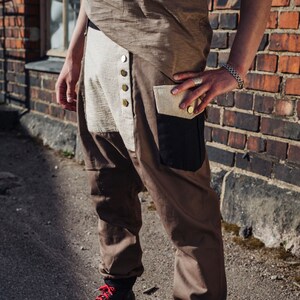 May include: Brown and tan pants with a unique design, featuring a button-up front and a black pocket. The pants are paired with black high-top sneakers with red laces. The outfit is casual and stylish.