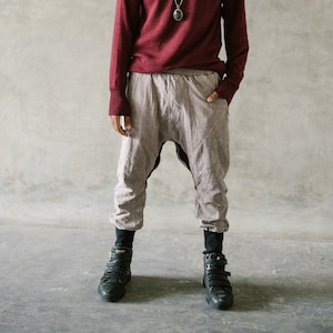 May include: A person wearing a burgundy long-sleeve sweater, light gray harem pants, and black high-top sneakers. A silver necklace with a pendant is visible. The outfit is casual and comfortable.