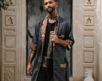 Puede incluir: Un hombre con una bata de cuadros azul y negro con un forro estampado en marrón y naranja. La bata tiene un cinturón y bolsillos. También lleva pantalones negros y botas negras.