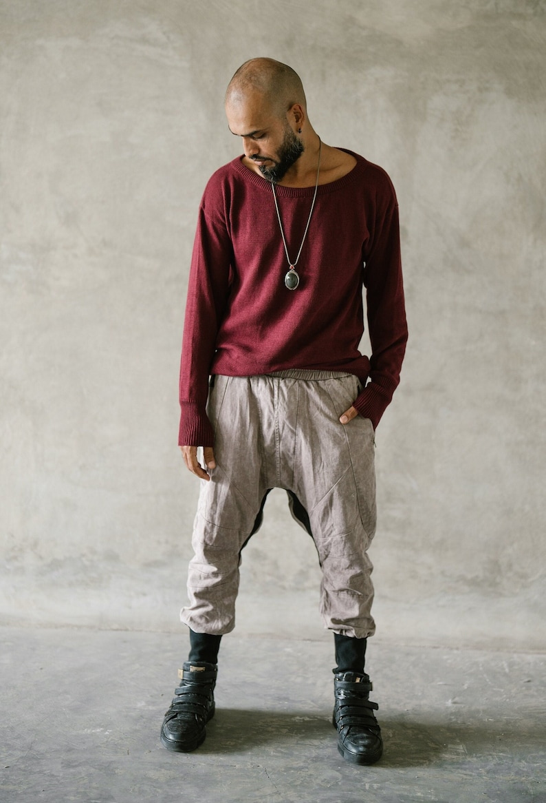 May include: A person wearing a burgundy long-sleeve sweater, light gray harem pants, and black high-top sneakers. A silver necklace with a pendant is visible. The outfit is casual and comfortable.