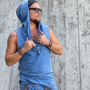 May include: A blue sleeveless hooded shirt with a drawstring hood. The shirt is made of a soft, comfortable fabric and has a relaxed fit. The model is wearing the shirt with a black beanie and sunglasses.