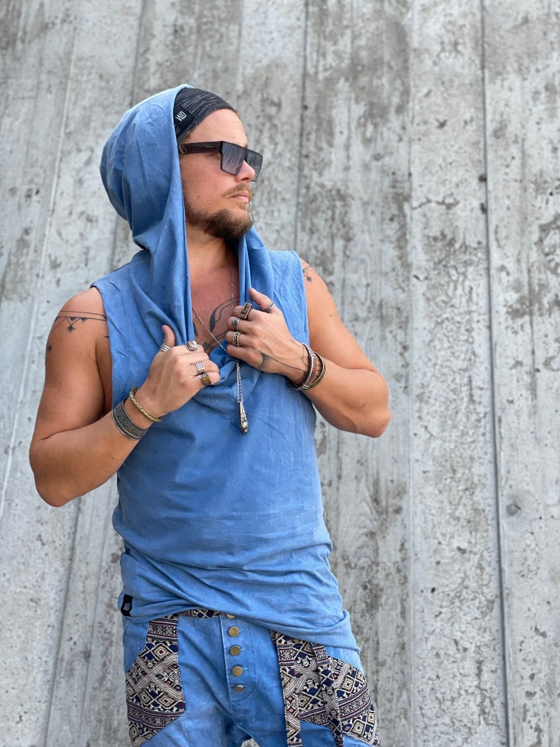 May include: A blue sleeveless hooded shirt with a drawstring hood. The shirt is made of a soft, comfortable fabric and has a relaxed fit. The model is wearing the shirt with a black beanie and sunglasses.
