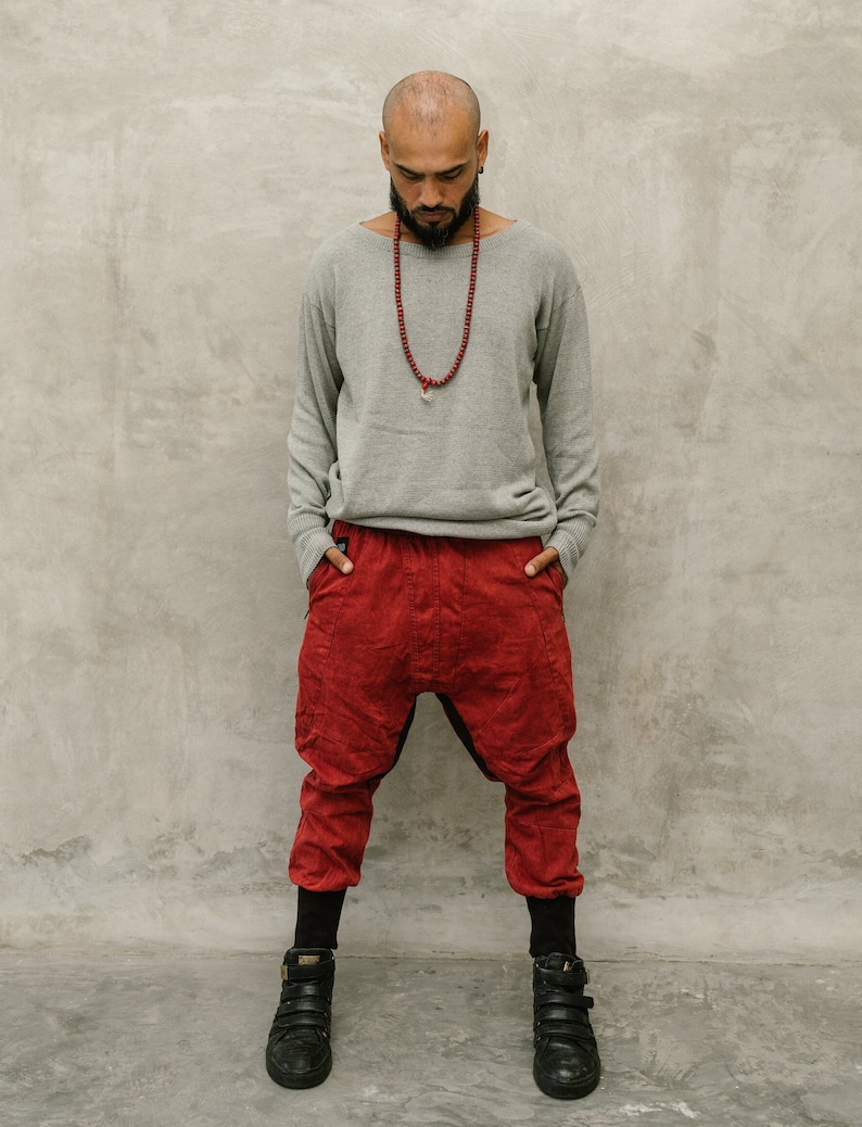 May include: A person wearing a gray long-sleeve sweater, red pants, black leggings, and black shoes. The red pants have a unique design. A red beaded necklace is worn around the neck.