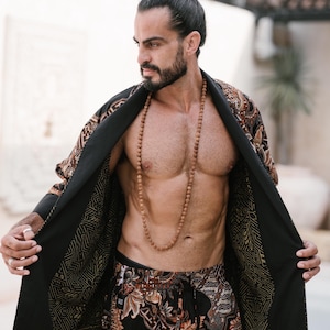 May include: A black and brown patterned robe with matching shorts. The robe has a geometric design on the edges and is open, revealing a wooden bead necklace. The shorts have a similar floral pattern.
