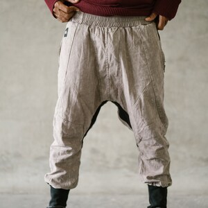 May include: A person wearing a burgundy sweater and light brown harem pants with black accents. The pants have a unique design with stitched details and are paired with black high-top sneakers with multiple straps.
