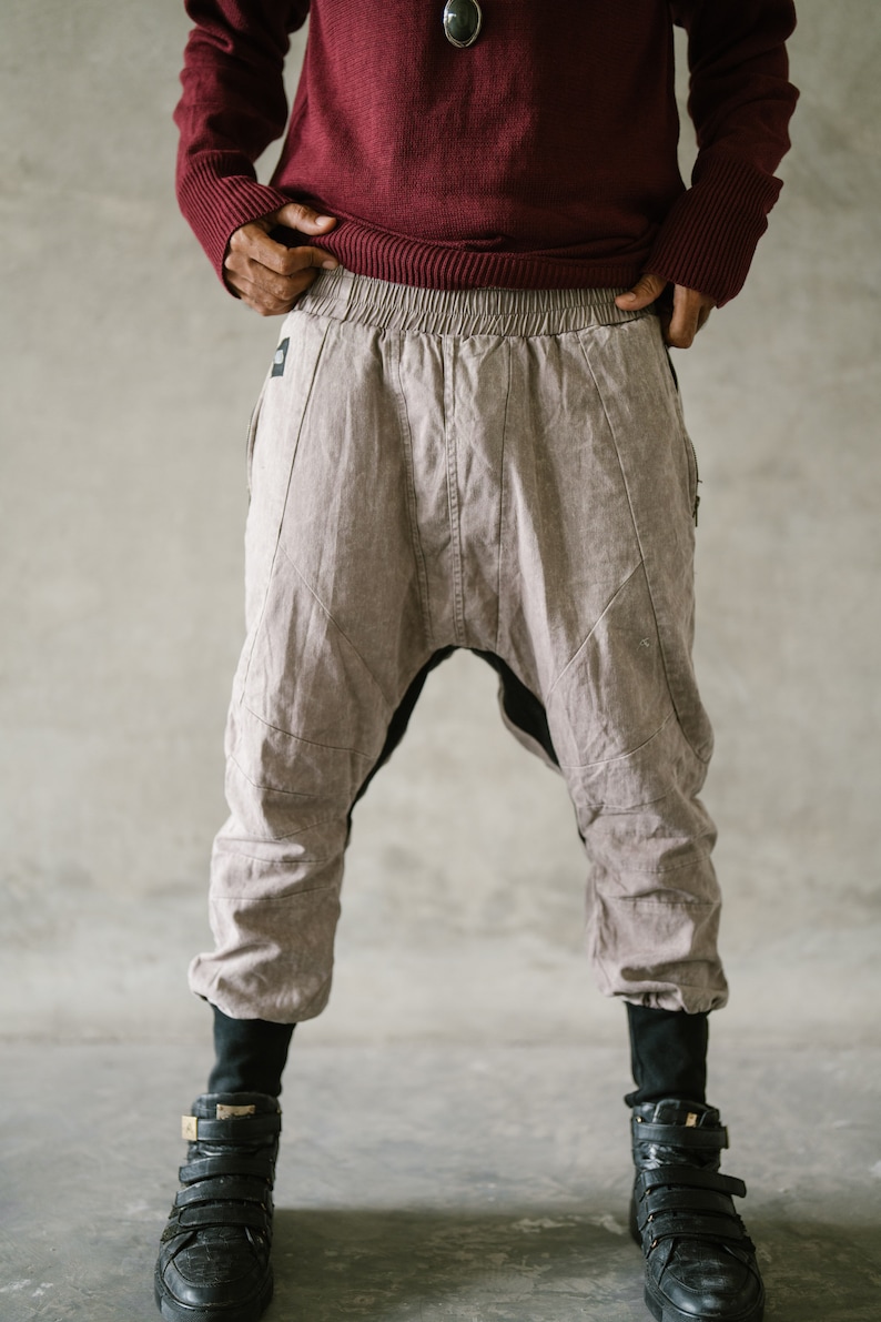 May include: A person wearing a burgundy sweater and light brown harem pants with black accents. The pants have a unique design with stitched details and are paired with black high-top sneakers with multiple straps.