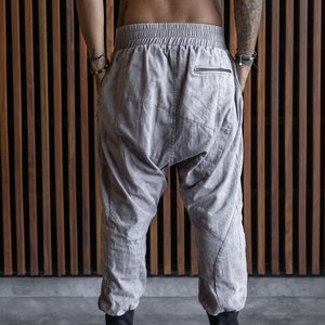 May include: Light gray harem pants with a drawstring waist and a zipper pocket on the back. The pants have black cuffs at the ankles and a relaxed fit. The pants are made of a soft, textured fabric.