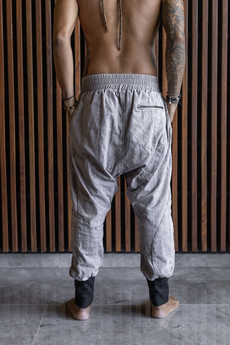 May include: Light gray harem pants with a drawstring waist and a zipper pocket on the back. The pants have black cuffs at the ankles and a relaxed fit. The pants are made of a soft, textured fabric.
