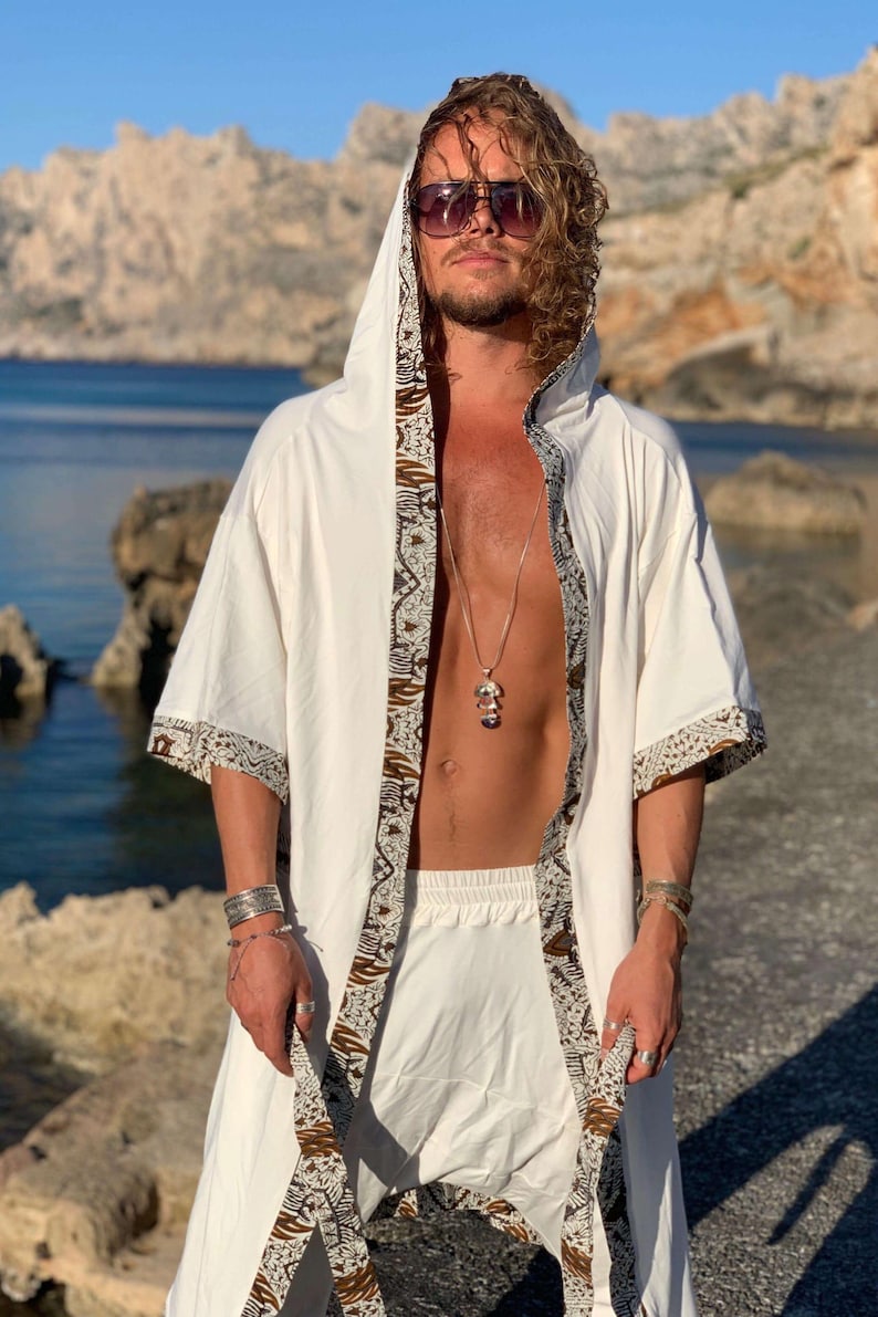 May include: A white hooded robe with brown and white patterned trim. The robe is open in the front and has a silver necklace with a pendant.