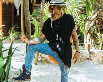 May include: A person wearing a black shirt with a long, flowing hem, blue jeans, and a wide-brimmed hat. They are standing in a tropical setting with palm trees and lush greenery.
