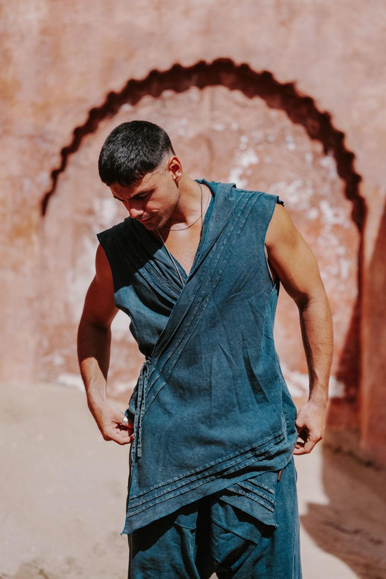 May include: A sleeveless, wrap-style top and matching pants in a muted teal color. The top features a draped design with pleats and a tie closure. The outfit is made of a soft, flowing fabric, perfect for warm weather.