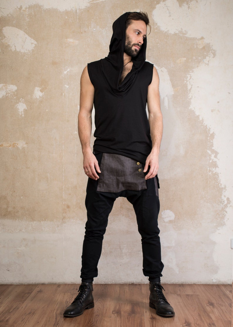 May include: Black hooded sleeveless top and black drop-crotch pants. The top has a cowl neck and a hood. The pants have a decorative panel with two buttons. The model is wearing black boots.