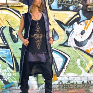 May include: A black sleeveless top with a gold geometric design, paired with black pants and a long hooded vest. The vest has a dark blue hood and a patterned lining. The outfit is completed with black boots. The background features colorful graffiti art.