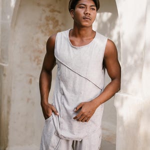 May include: A person wearing a light grey sleeveless shirt with a diagonal seam detail and matching light grey shorts. The person is standing in a doorway with a white wall behind them.