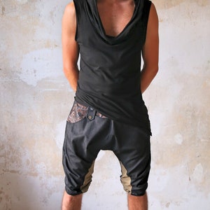 May include: A person wearing a black sleeveless hooded top with a cowl neck and black and brown pants. They are wearing brown leather boots.