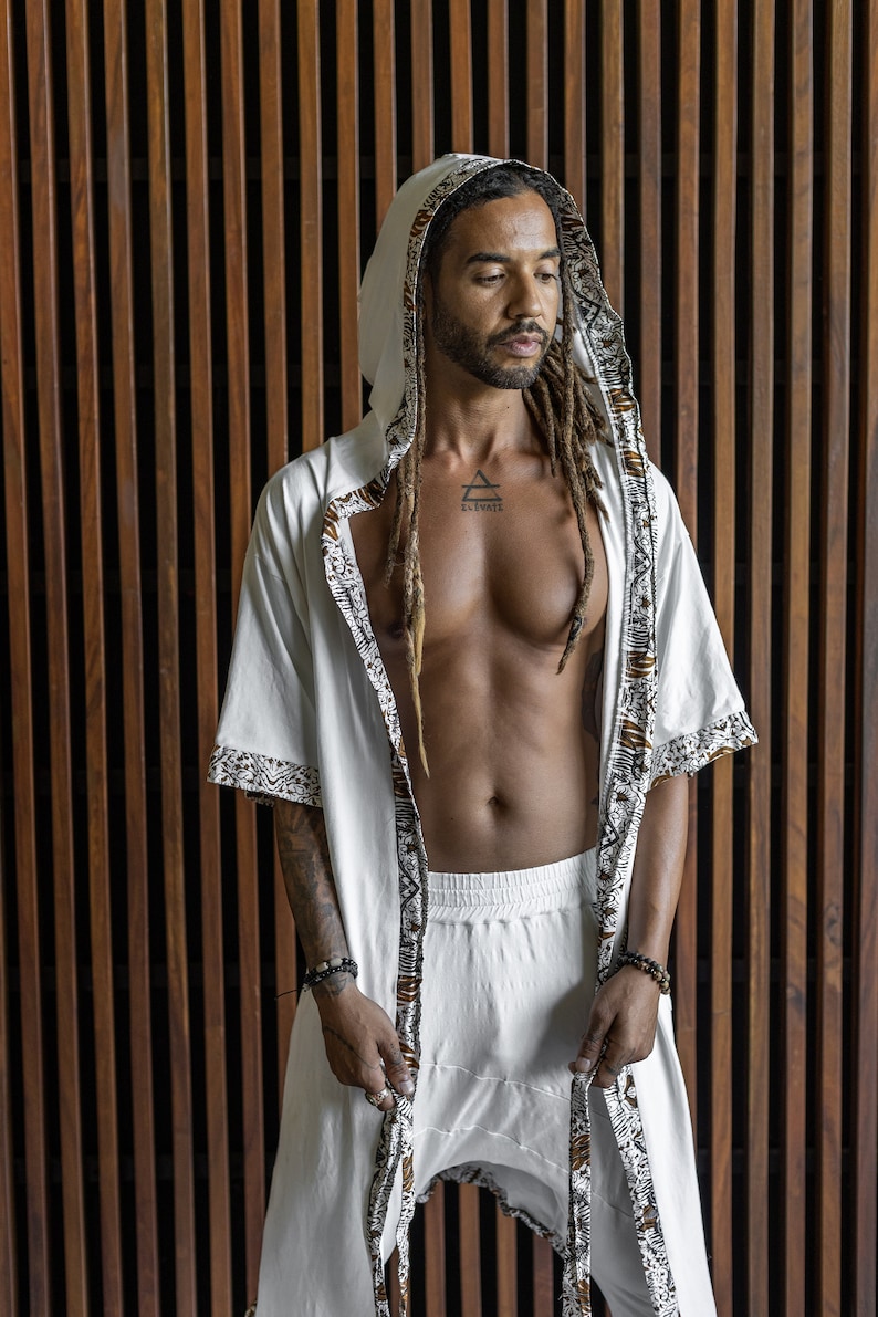 May include: A white hooded robe with brown and white patterned trim. The robe is open in the front, revealing a white undershirt and a tattoo on the chest that reads "Elevate".
